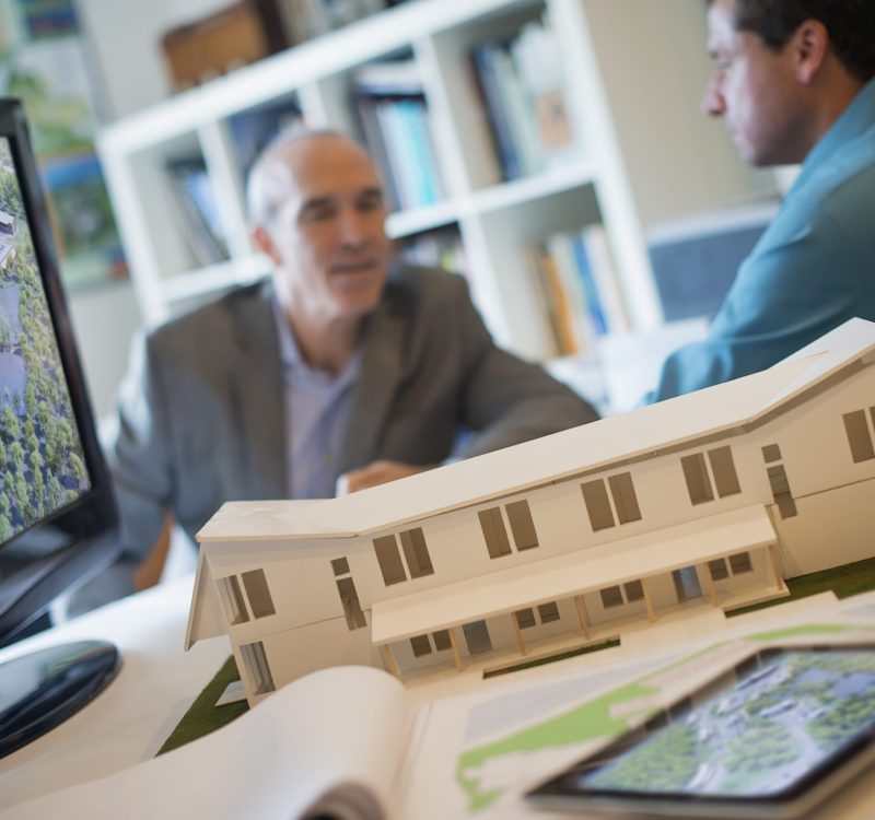 Architects working on a green construction project, using computer technology, in an office. Scael model of a building.