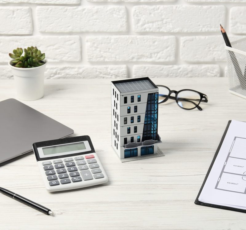Real estate. Apartment building model, floor plan, calculator and laptop on white wooden table
